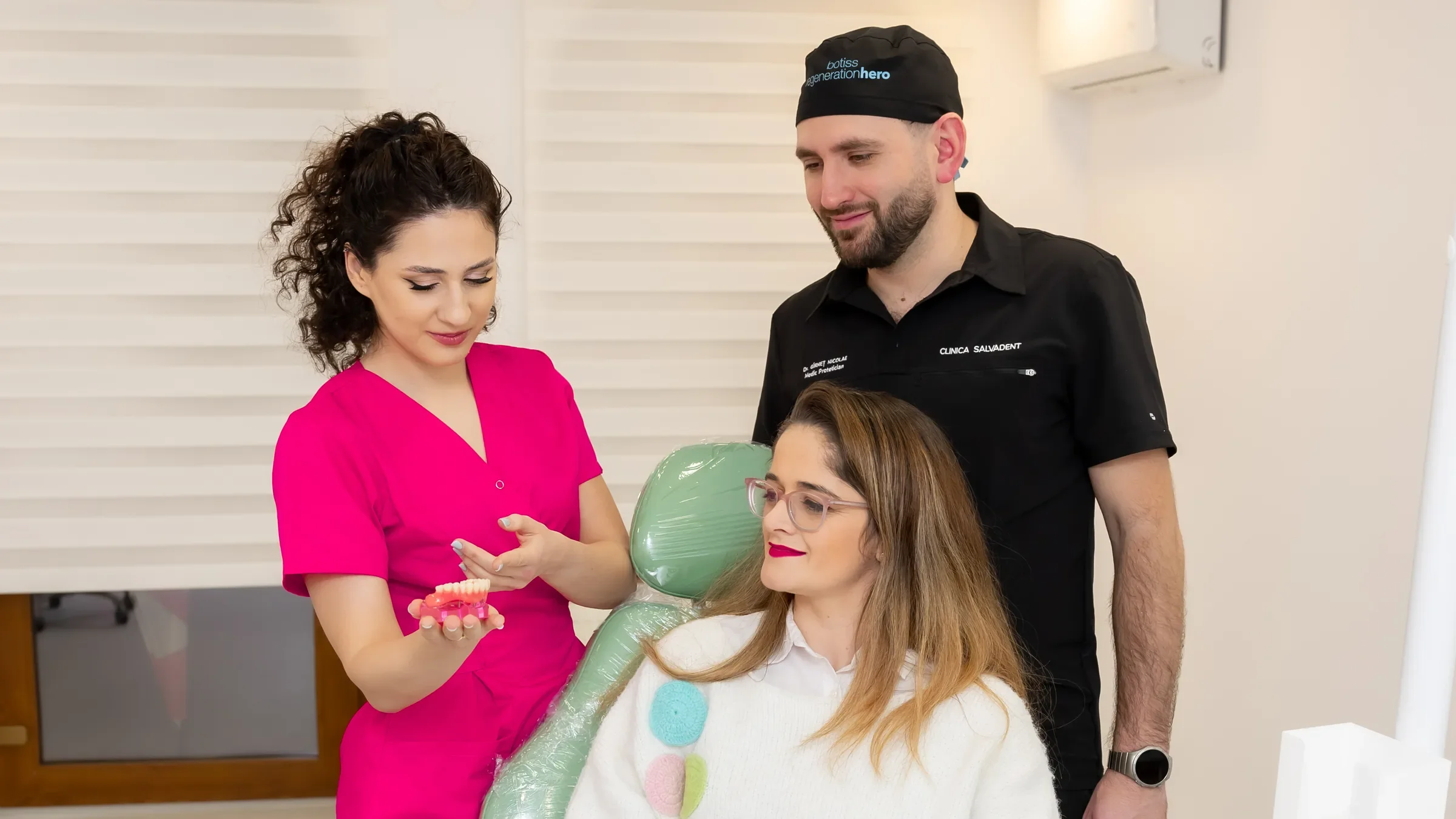 Medic SalvaDent care îi arată unei paciente un model dentar, cu un coleg alături